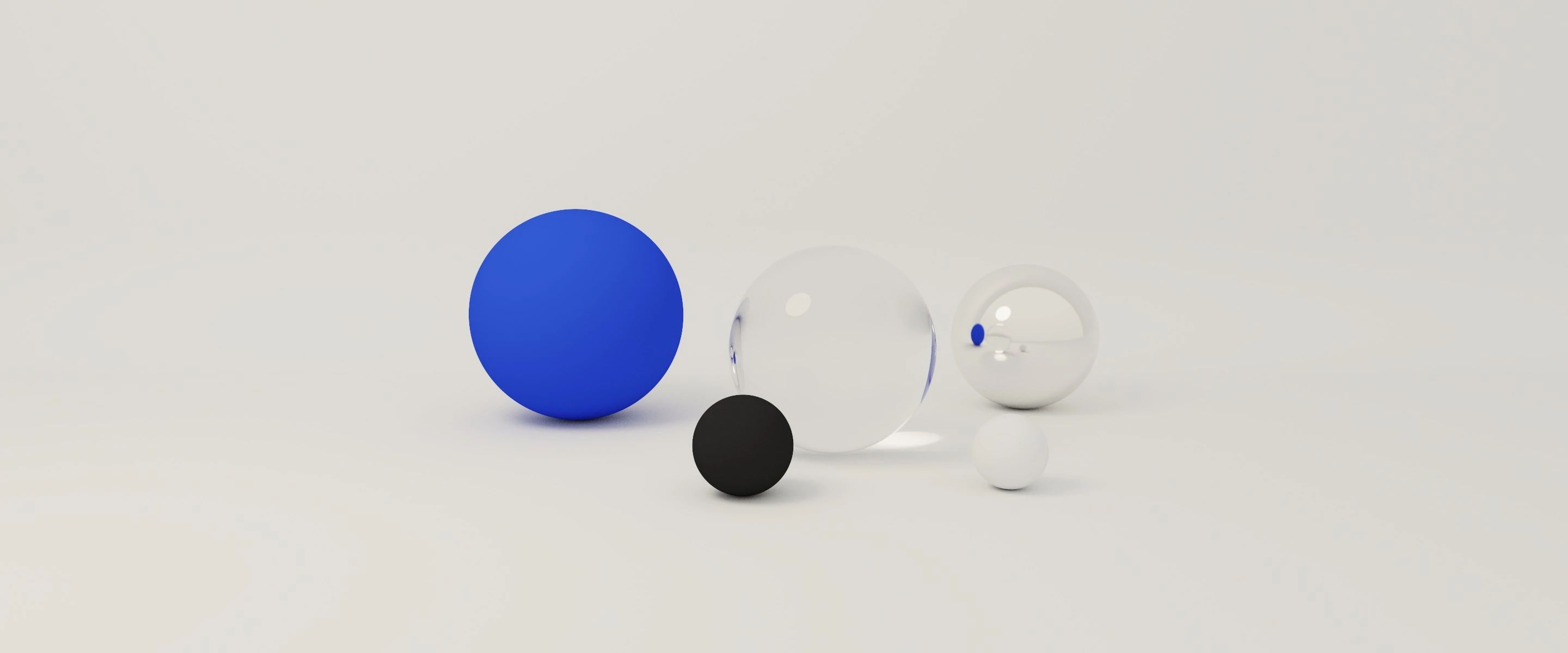 A path-traced render in a white studio: a matte cobalt sphere, a glass sphere, a chrome sphere, a small black sphere and a small white sphere, lit by one soft light.